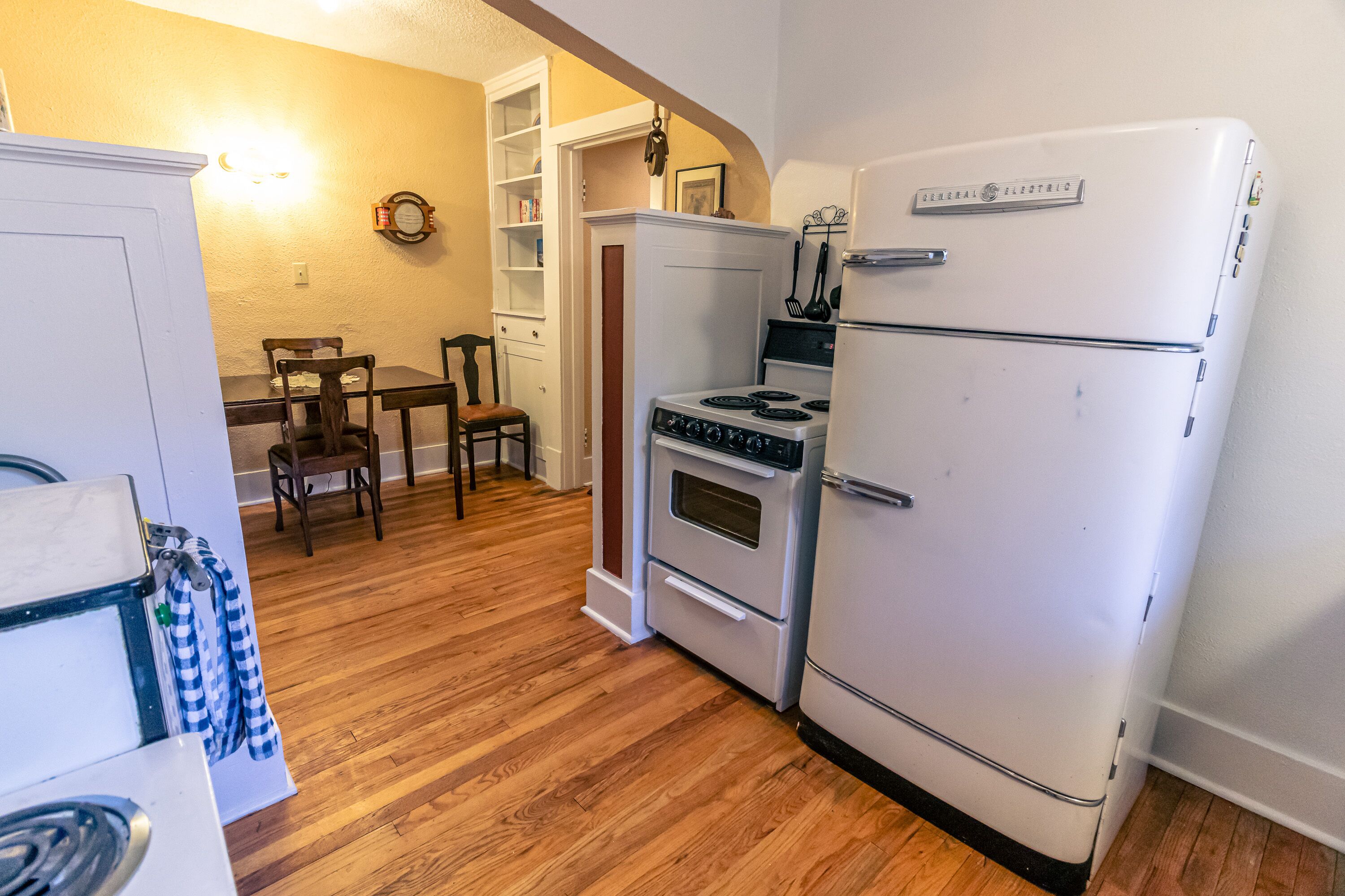 A kitchen with a white refrigerator, stove, and oven, wooden floor, and a dining table with chairs.