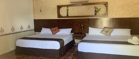 Habitación de hotel con dos camas, un ventilador de techo, una mesita de noche y un estante en la pared con plantas.
