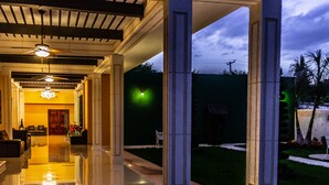 Un espacio exterior cubierto con piso reflectante, columnas y un candelabro.