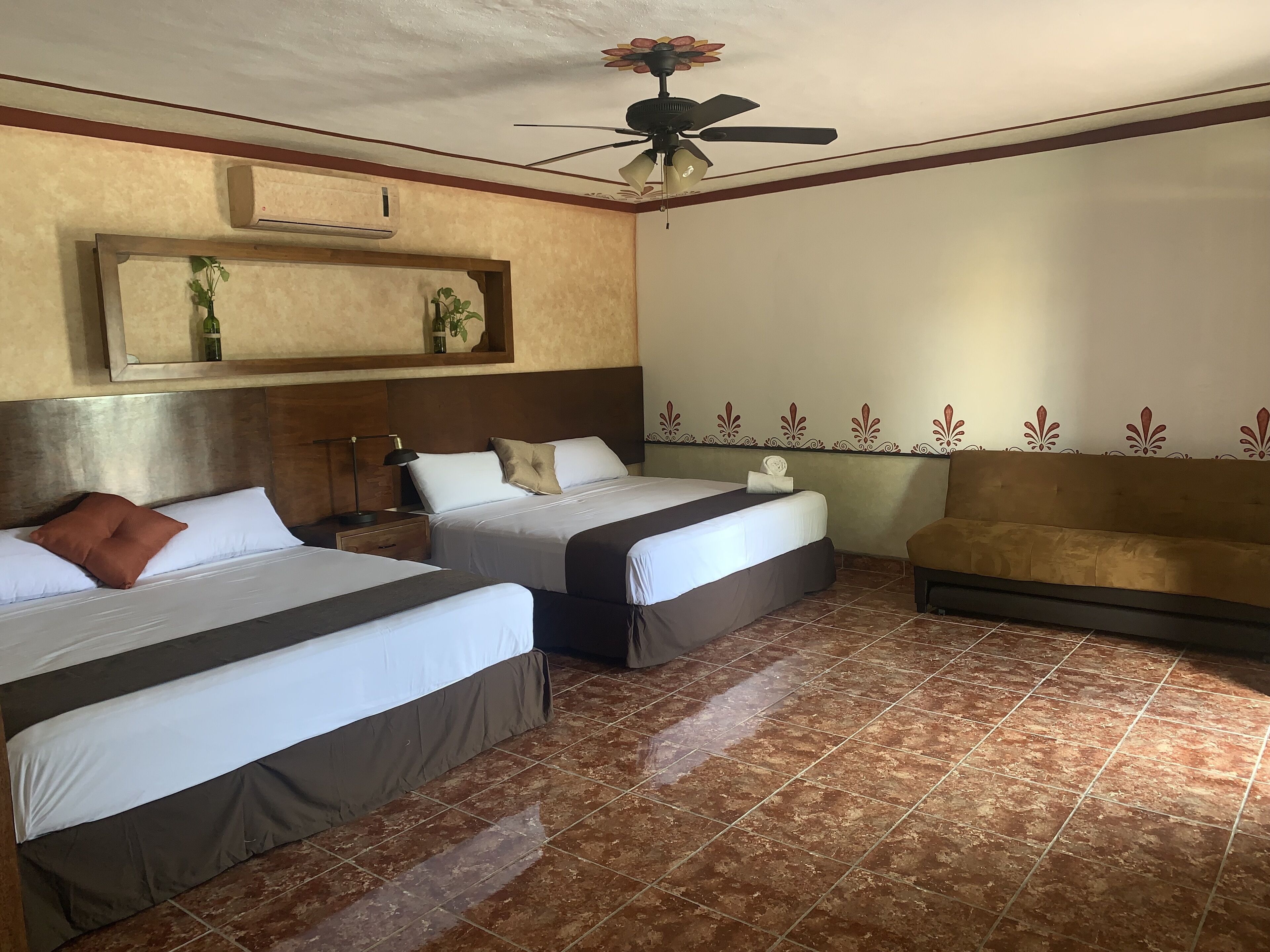 Une chambre d’hôtel avec deux lits, un ventilateur de plafond, un canapé et un panneau décoratif mural.