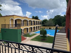 A courtyard with a pool, a two-story building with arched balconies, and a staircase leading to a balcony. - Hotel Tuul (Izamal)