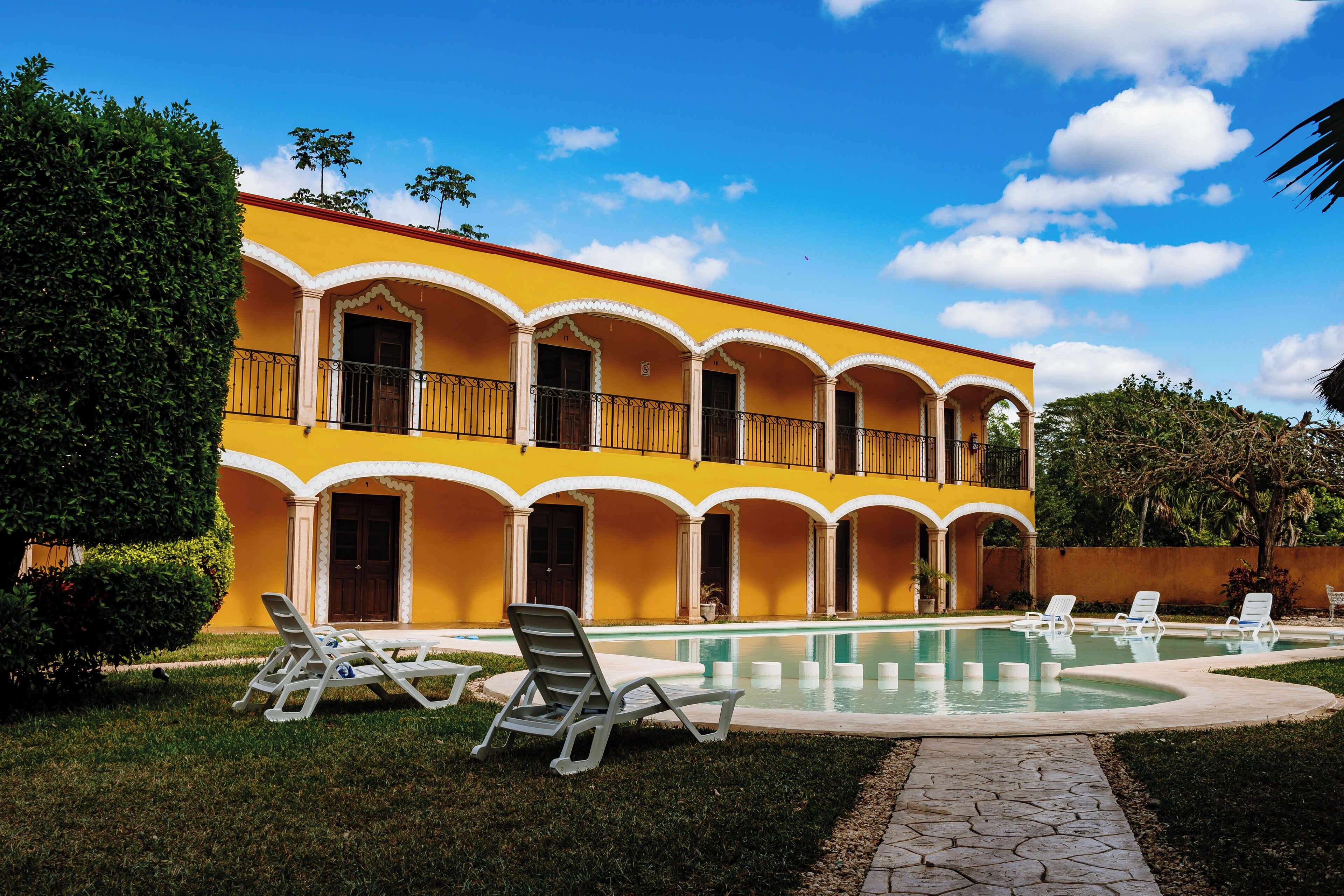Un bâtiment jaune avec une piscine et des chaises longues.