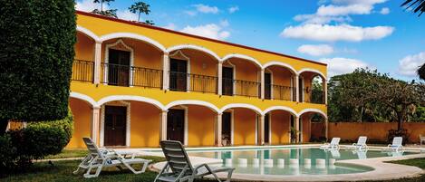 A yellow building with a swimming pool and lounge chairs.