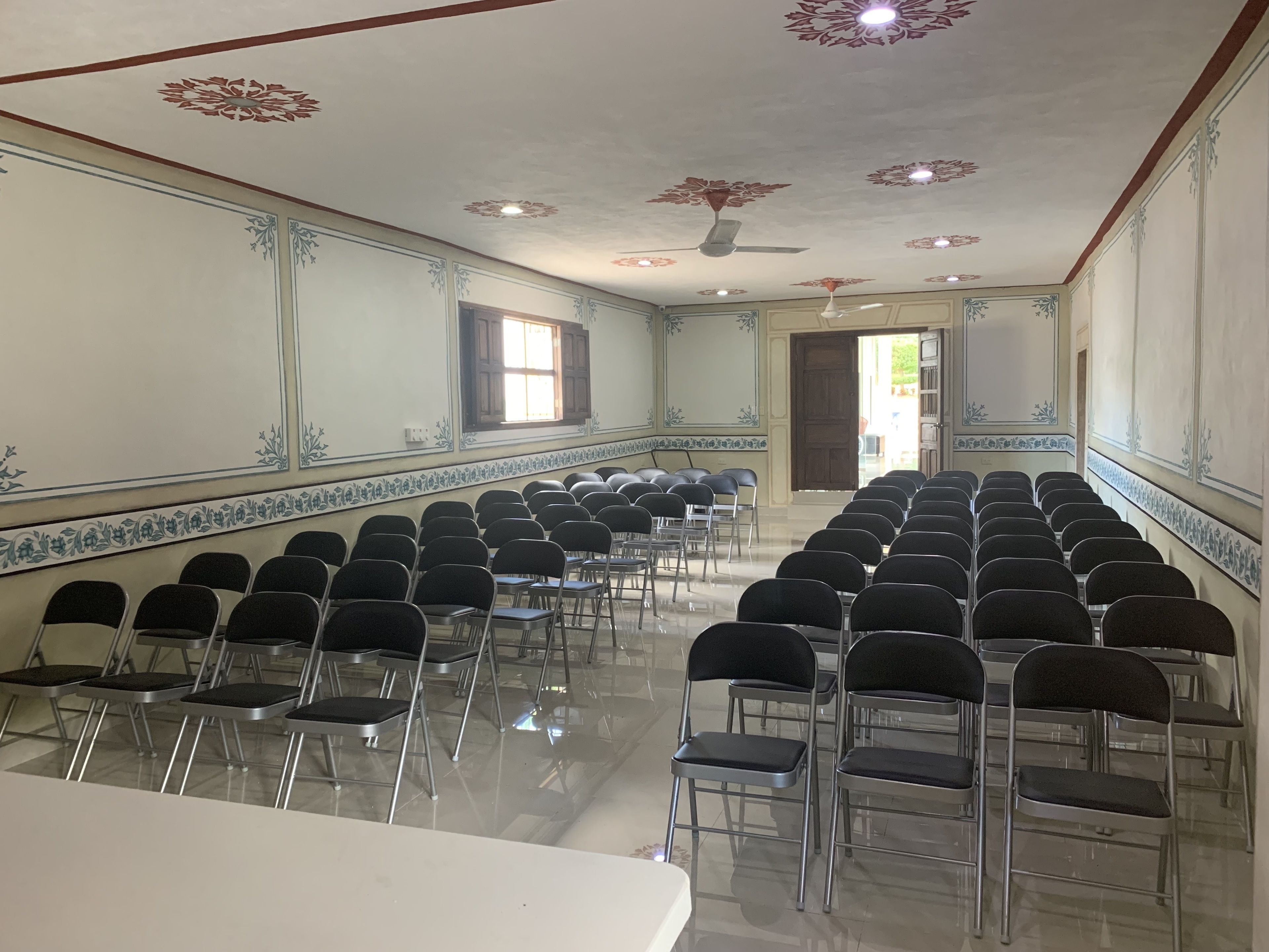 Un salón de conferencias con filas de sillas, una mesa blanca y detalles decorativos en el techo.