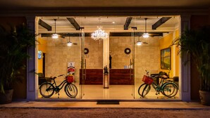 Entrada de un hotel con una araña, dos bicicletas y un mostrador de recepción.