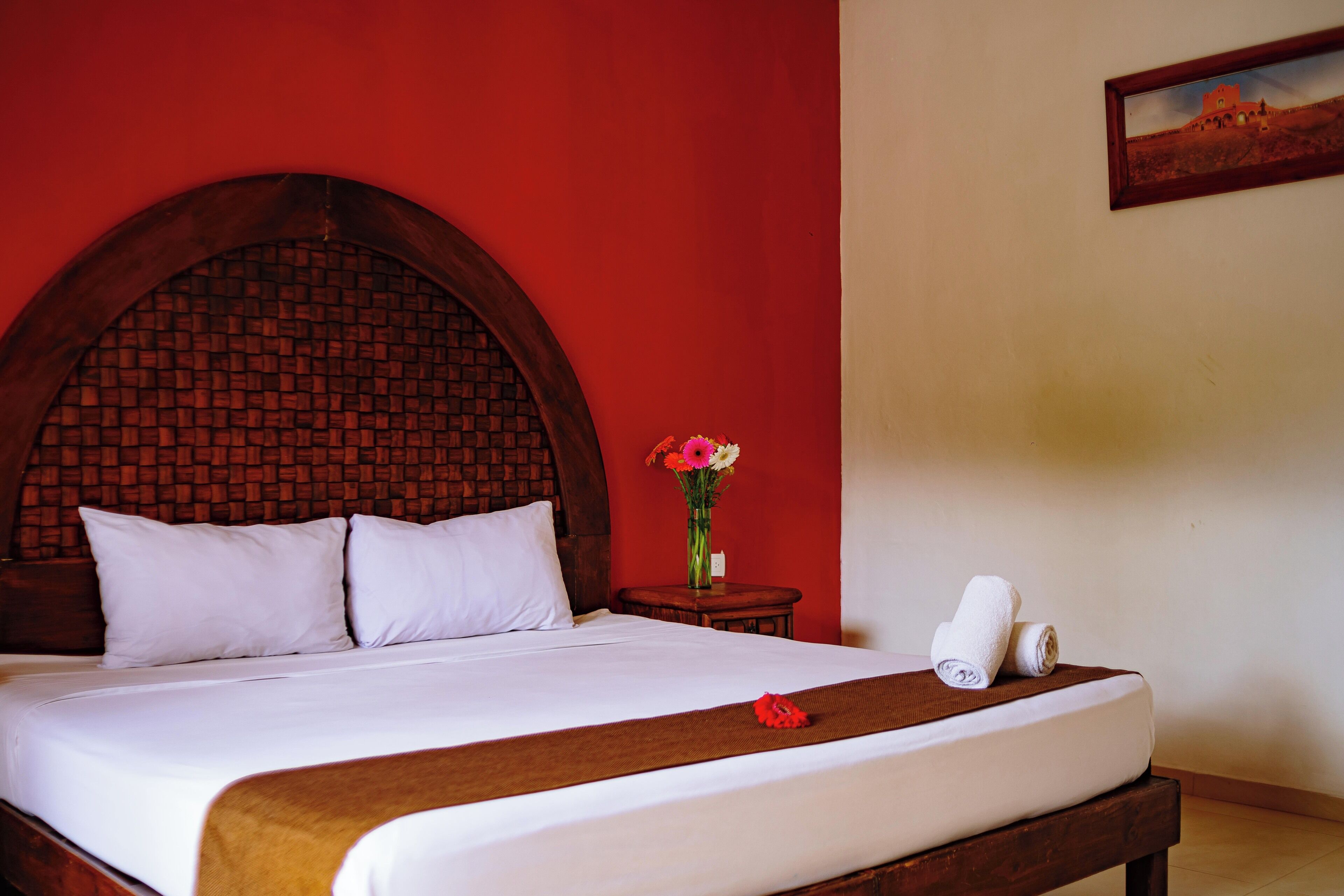 A neatly made bed with white linens, a wooden headboard, and a small table with a vase of flowers.