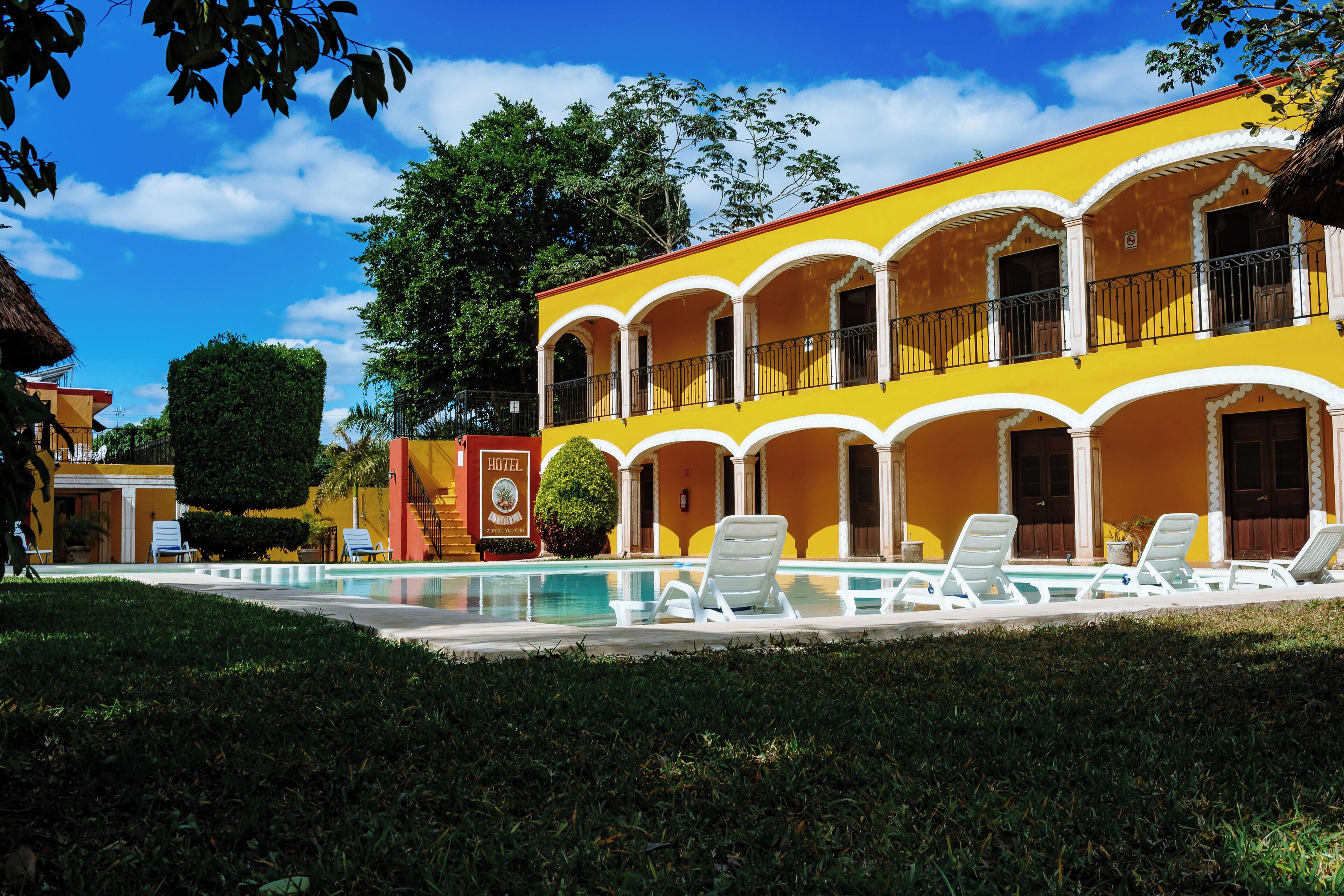 A yellow building with a swimming pool and lounge chairs.