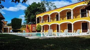 A yellow building with a swimming pool and lounge chairs.