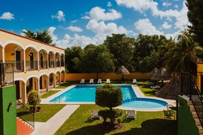 A pool area with a clear blue pool, white lounge chairs, and a thatched umbrella. - Hotel Tuul (Izamal)