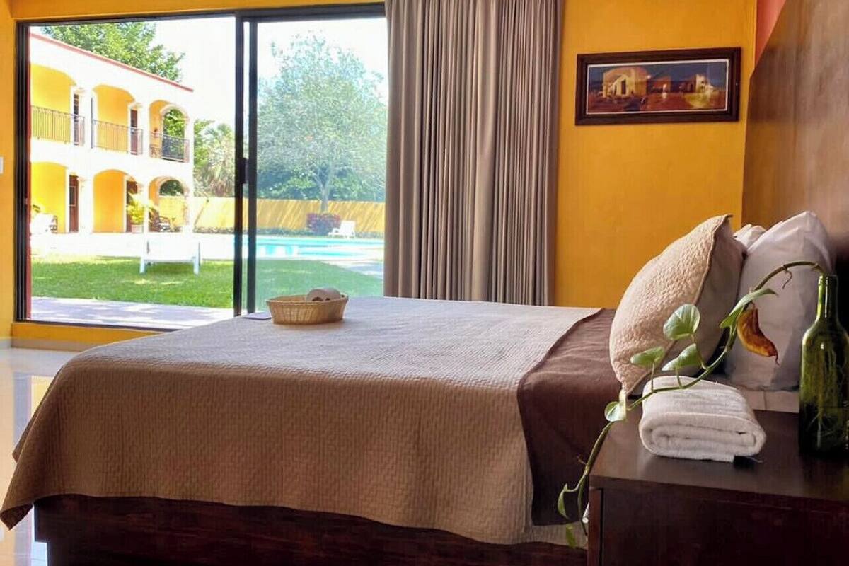 A bedroom with a large bed, a nightstand, a window with curtains, and a view of a pool and building outside.
