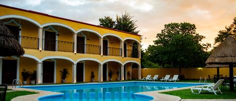 A hotel with a swimming pool, outdoor seating, and a thatched-roof structure.