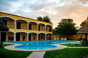 A hotel with a swimming pool, outdoor seating, and a thatched-roof structure. - Hotel Tuul (Izamal)