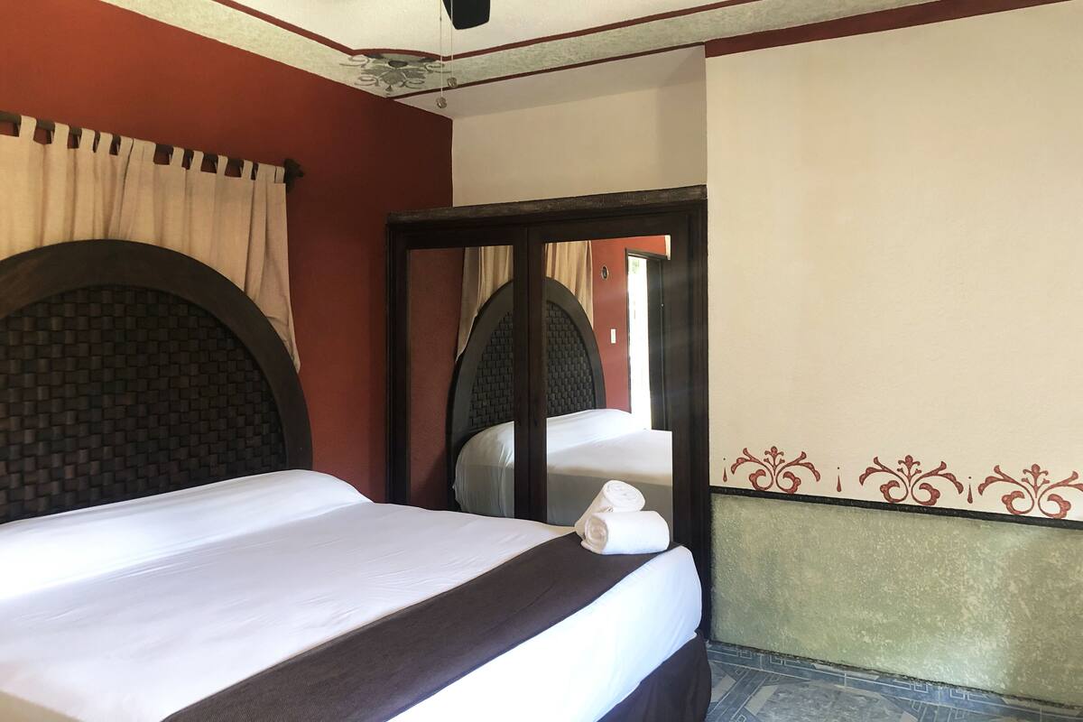 A hotel room with a bed, a ceiling fan, a mirror, and a door.