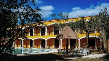 A hotel with a swimming pool, outdoor seating, and a thatched-roof structure.