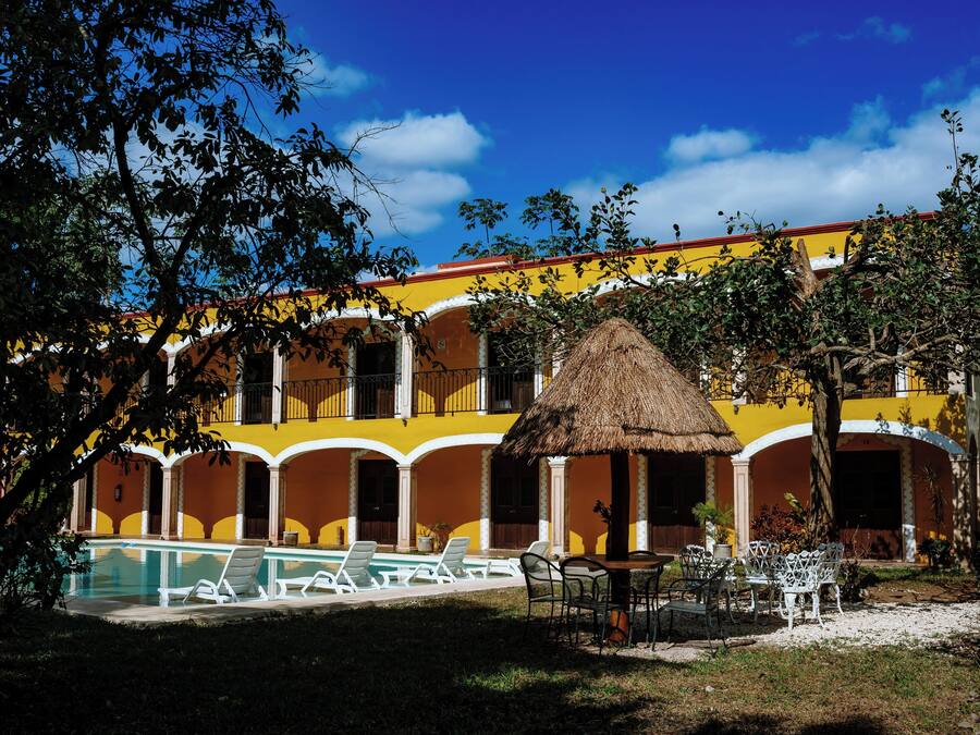 A hotel with a swimming pool, outdoor seating, and a thatched-roof structure.