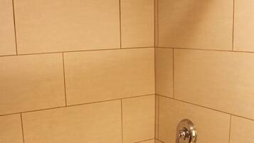 Un baño con baldosas color beige, una bañera blanca y un cabezal de ducha.
