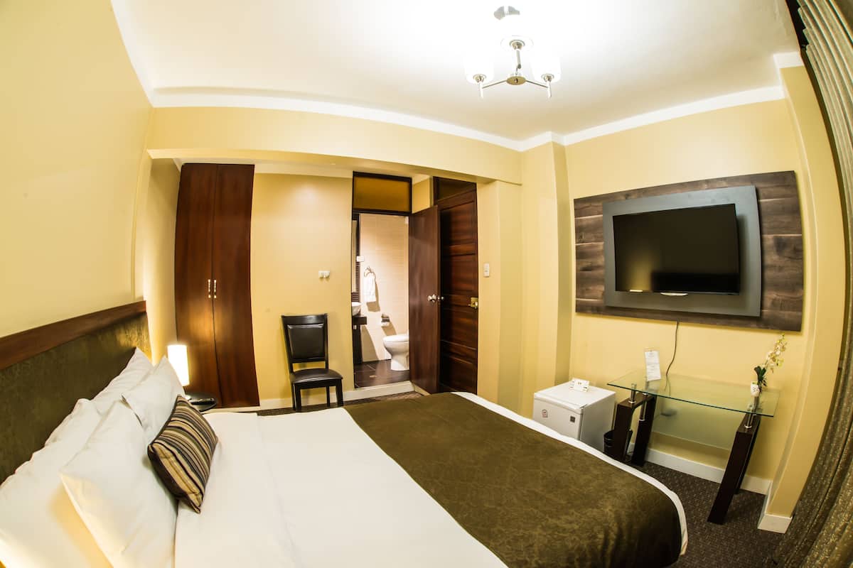 Ein Hotelzimmer mit einem großen Bett, einem an der Wand montierten Fernseher, einem Schreibtisch mit Computer und einem Stuhl.