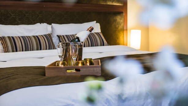 A neatly made bed with a bottle of champagne, glasses, and small bottles on a tray. - Los Leones Hotel Boutique (Arequipa)