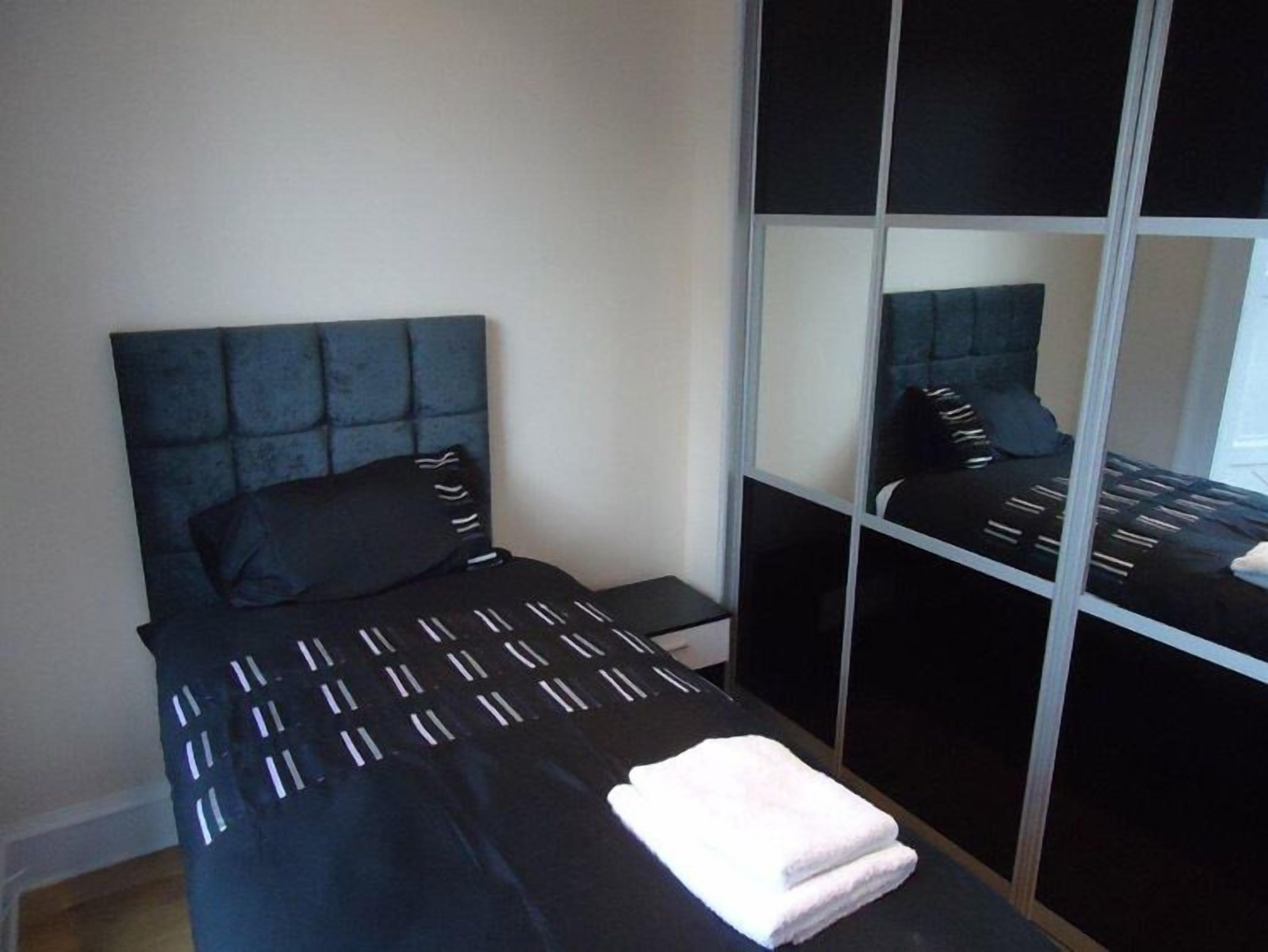 Un dormitorio con cama, mesita de noche, espejo y ventana.