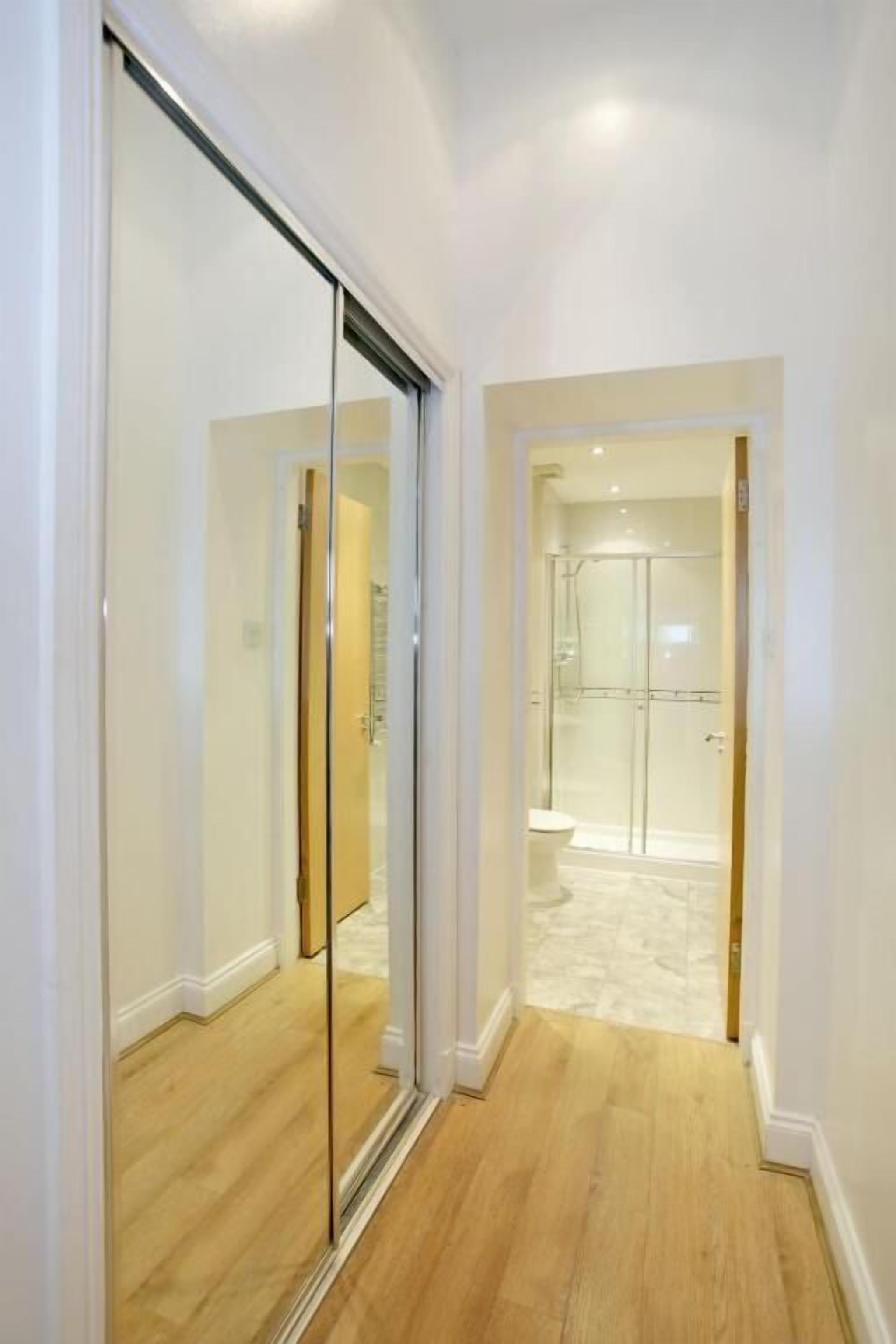 A hallway with a glass door leading to a bathroom with a shower and toilet.