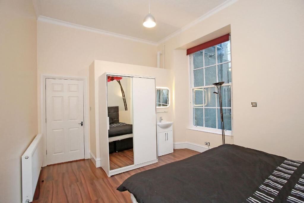 A bedroom with a bed, a wardrobe, a mirror, a window, and a radiator.