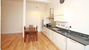 Una cocina moderna con comedor, sillas de madera, un lavamanos de acero inoxidable y un reloj en la pared.
