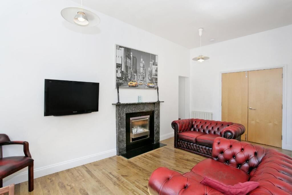 A living room with a fireplace, a television mounted on the wall, a red leather sofa, and a wooden door.