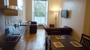 Una cocina moderna con estufa, lavamanos y armarios. Hay una zona de comedor con una mesa y sillas, y un ventanal que proporciona luz natural.