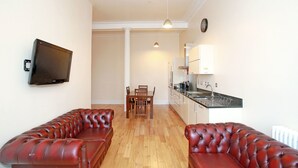 Una sala de estar con sofá, televisión, mesa de comedor y zona de cocina.