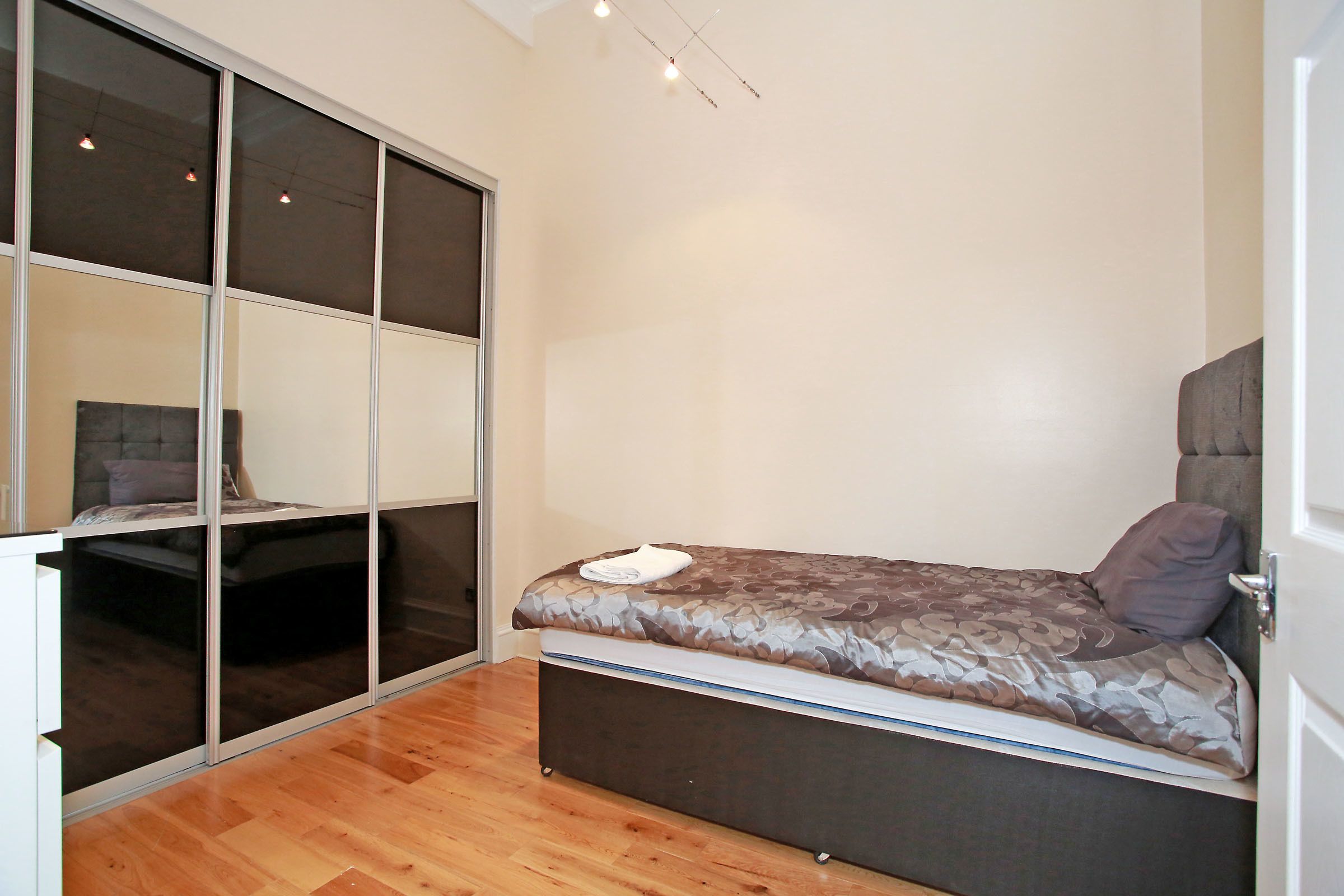 A compact bedroom with a bed, a sliding door closet, and a wooden floor.