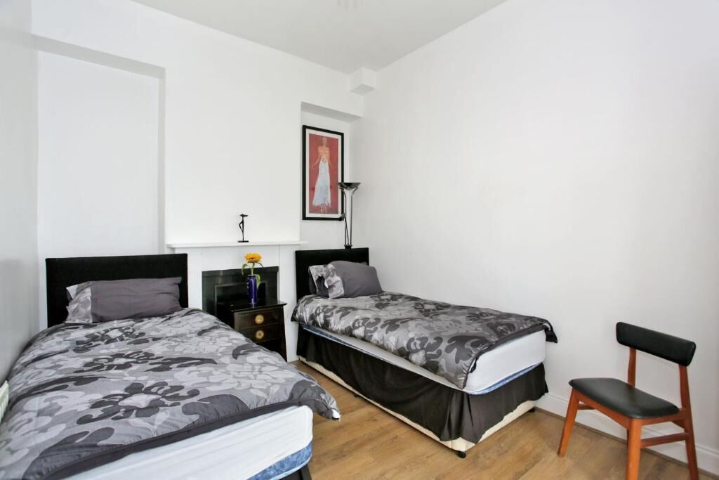 A bedroom with two beds, a nightstand, a chair, a framed picture on the wall, and a floor lamp.