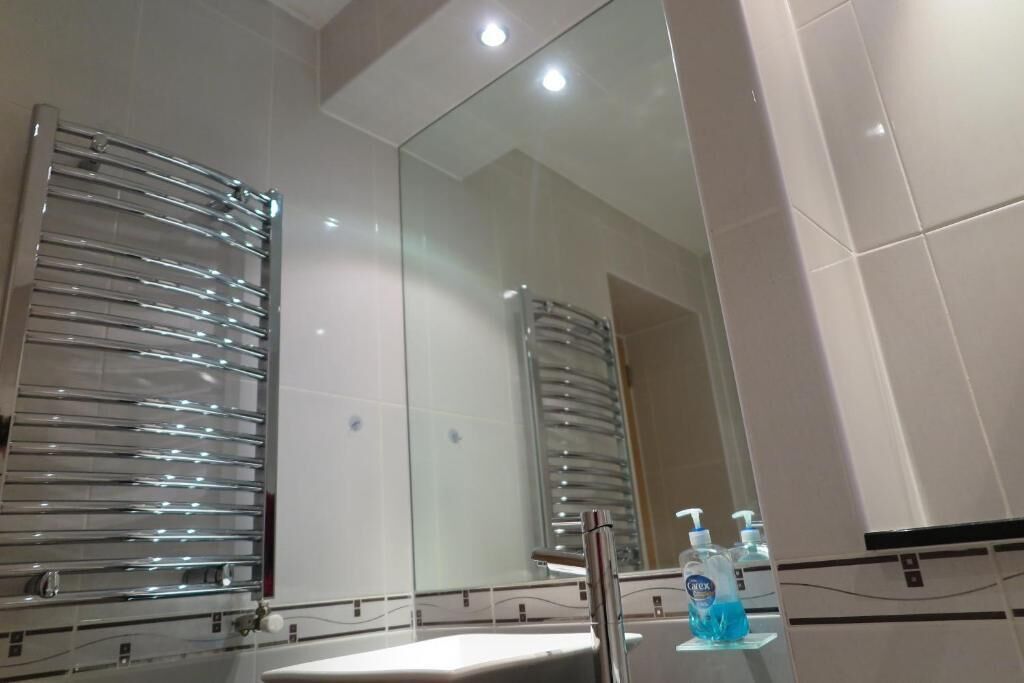 A bathroom with a large mirror, chrome towel racks, a sink, and a glass shower enclosure.