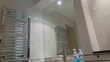 A bathroom with a large mirror, chrome towel racks, a sink, and a glass shower enclosure.