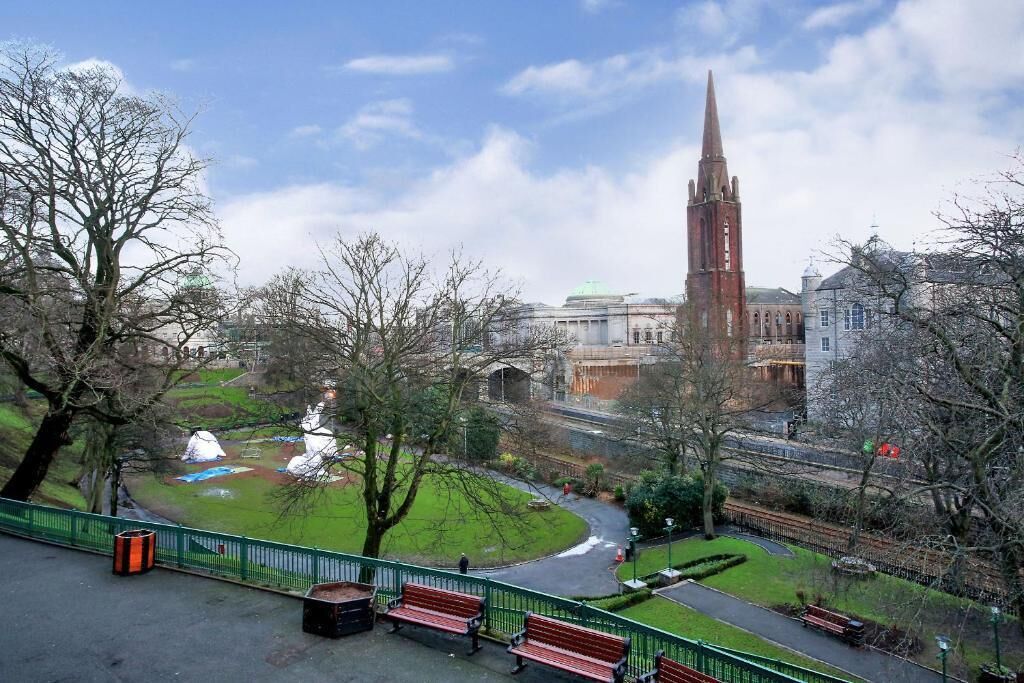 A park with benches, a pathway, and a historic building with a tall tower.