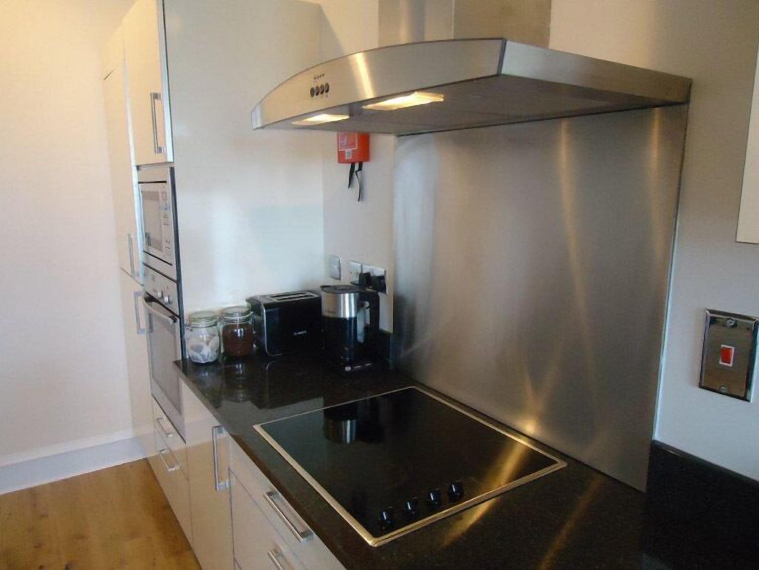 Una cocina moderna con una campana extractora de acero inoxidable, un horno empotrado, un tostador y una cafetera sobre la encimera.