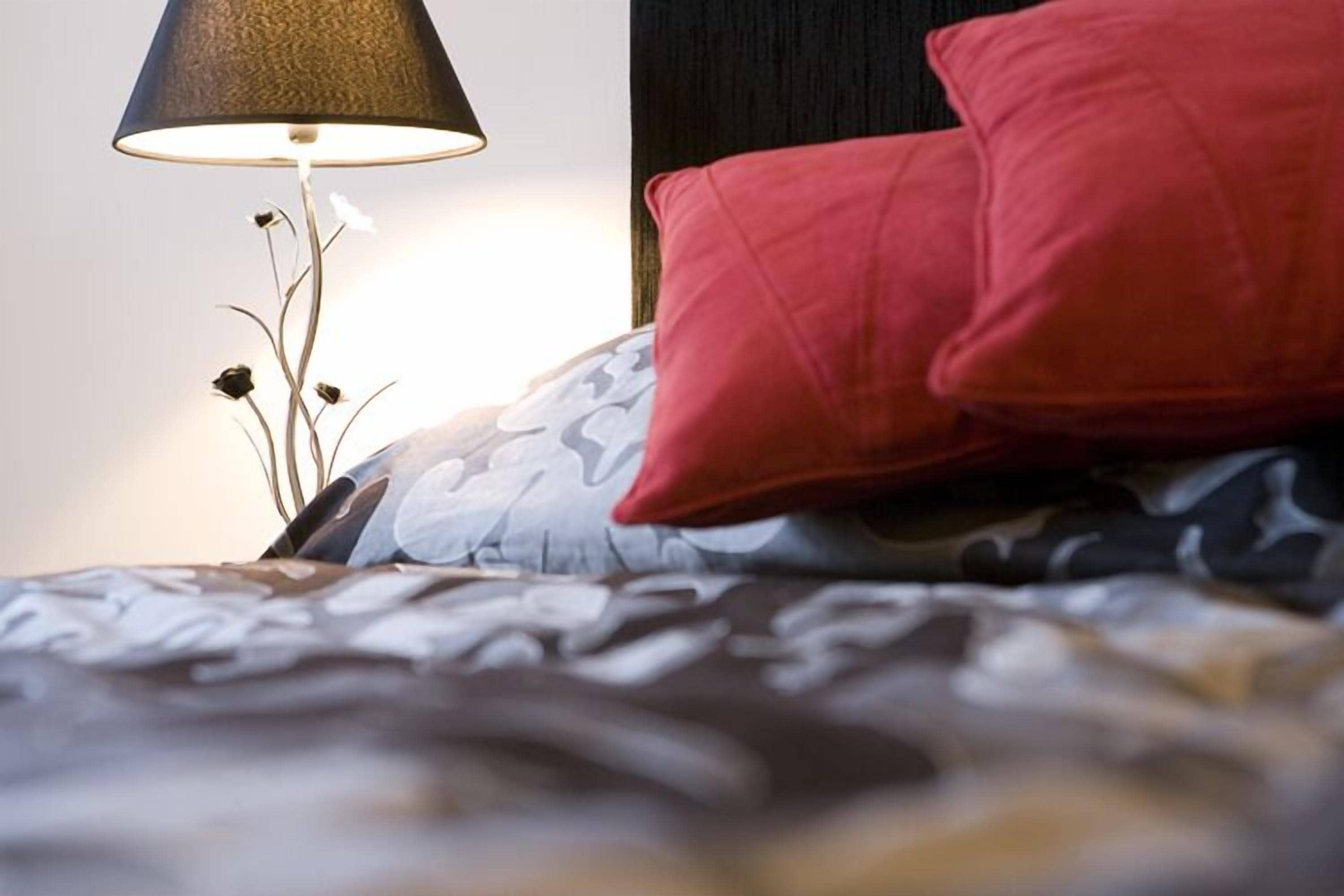A bed with a patterned bedspread and a red pillow.