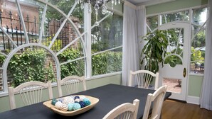 A dining area with a table set for four, surrounded by white chairs, large windows with a view of greenery, and a chandelier. - The Natchez Pearl (Natchez)