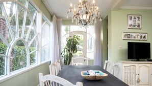 A dining area with a dark table, white chairs, a chandelier, and a window with curtains. - The Natchez Pearl (Natchez)
