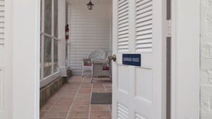 A corridor with a closed door labeled "Carriage House," a wicker chair, and a hanging lantern. - The Natchez Pearl (Natchez)