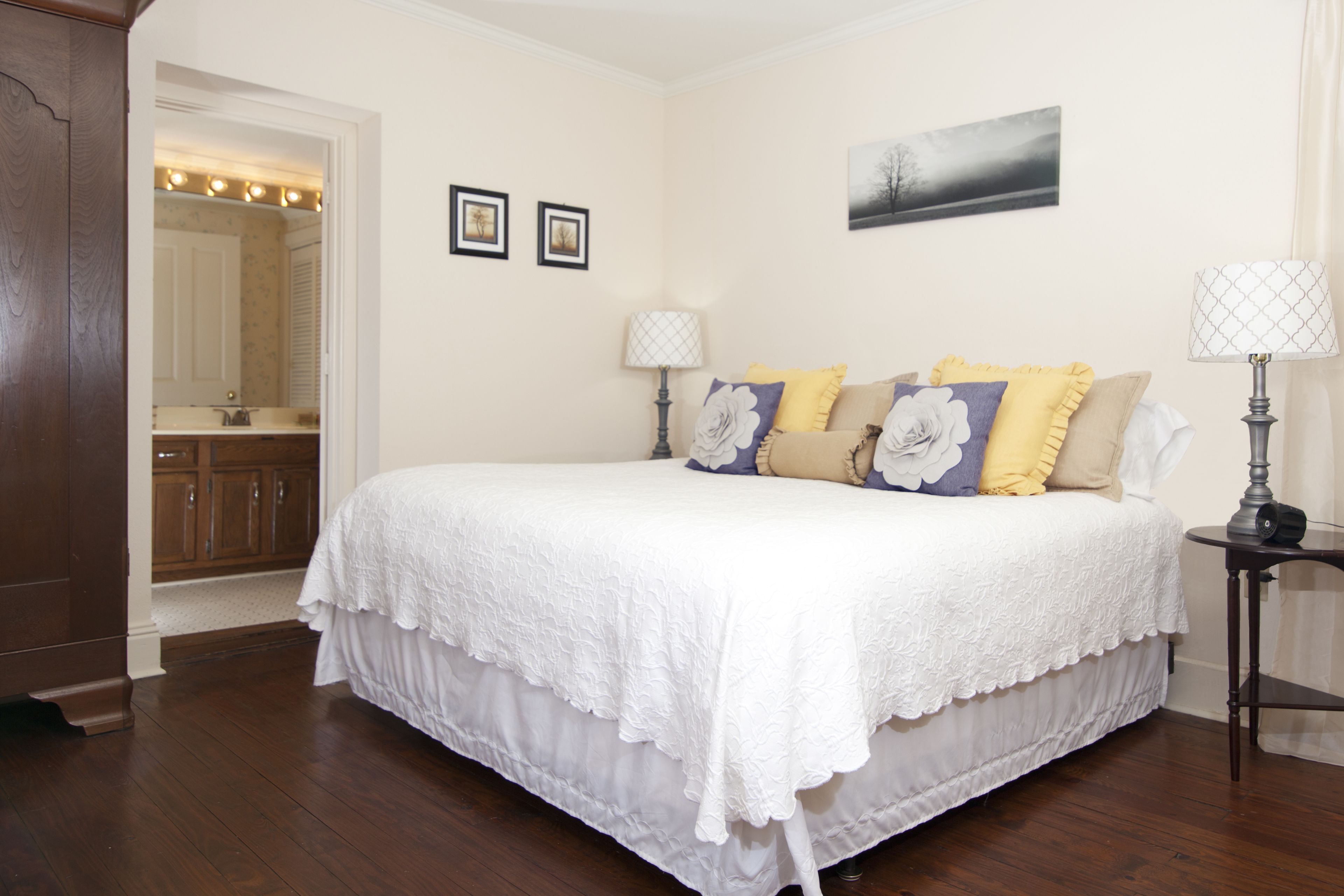 A bedroom with a large bed, two bedside lamps, a nightstand, a dresser, and a mirror.