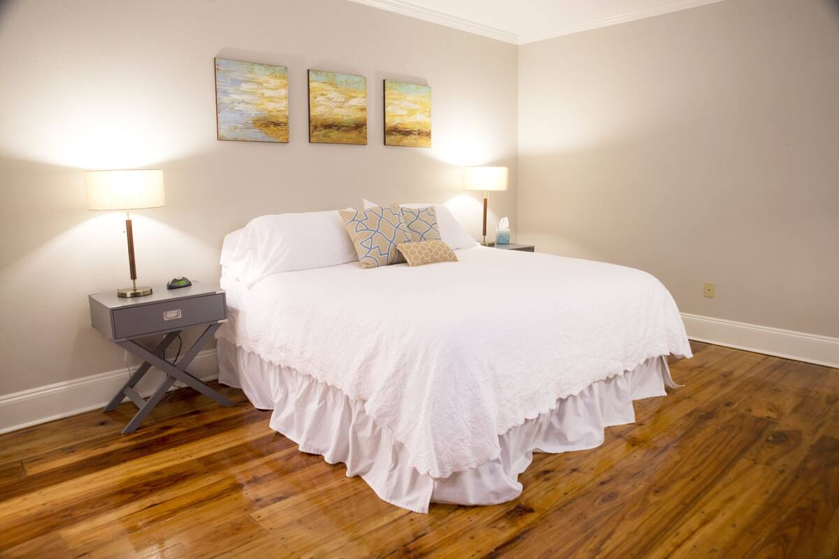 A bedroom with a large bed, two bedside tables with lamps, and three wall-mounted paintings.
