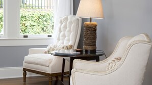 A room with two upholstered chairs, a small table with a lamp, and a window with a view of greenery outside. - The Natchez Pearl (Natchez)