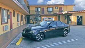 A black BMW parked in front of a yellow building with a fire escape, a garage, and a signboard. - Satellite Motel (Los Angeles)