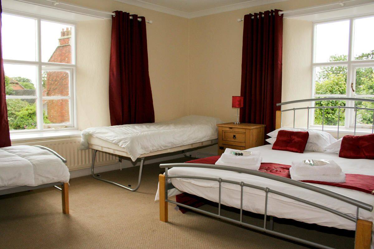 A room with two single beds, a wooden nightstand, a red lamp, and a window with red curtains.