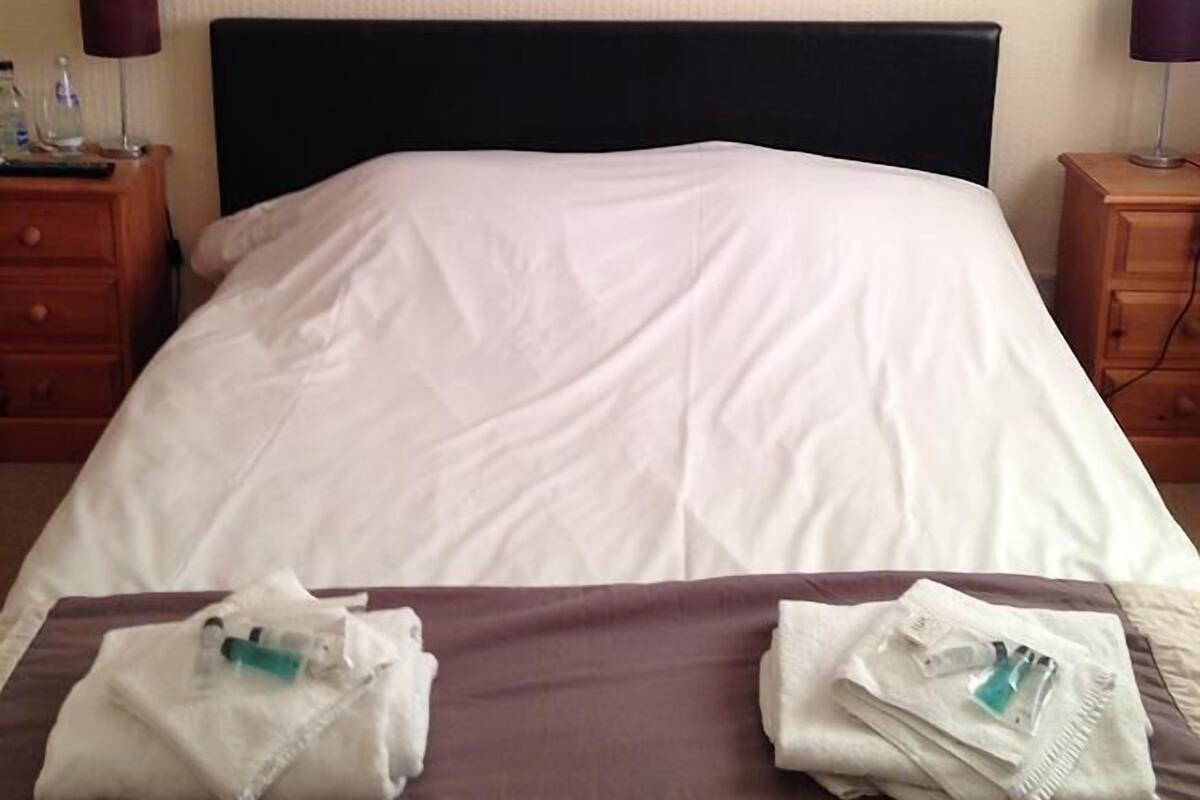 A hotel room with a bed, two nightstands, a painting on the wall, and towels on the bed.