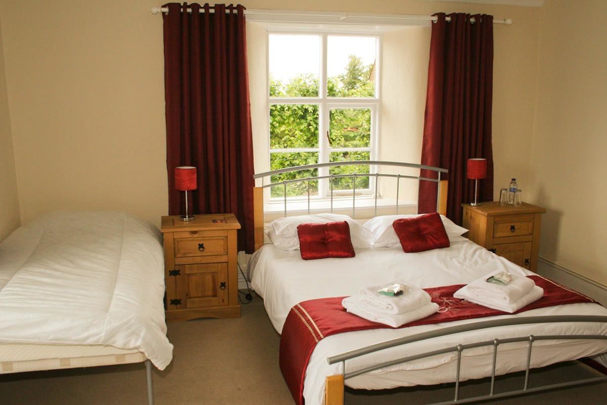 A double room with two beds, a window with curtains, and a view of greenery.
