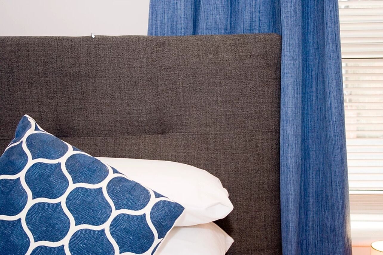 Una cama con cabecera oscura, un cojín de diseño azul y blanco, y un cojín blanco.