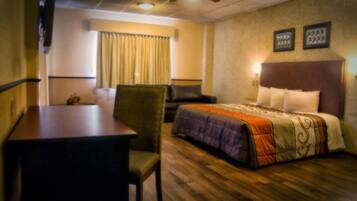 A hotel room with a bed, a desk, a chair, a window with curtains, and a wall with framed pictures.
