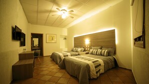 Habitación de hotel con dos camas, un escritorio, una silla, un ventilador de techo y un televisor montado en la pared.