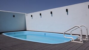 Una piscina rectangular con un borde blanco y una escalera metálica sobre un muelle de madera.